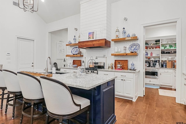 kitchen with a center island with sink, a breakfast bar area, light stone counters, white cabinetry, and stainless steel appliances