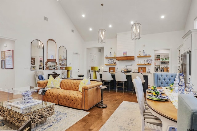 living room with built in shelves, an inviting chandelier, high vaulted ceiling, and hardwood / wood-style flooring