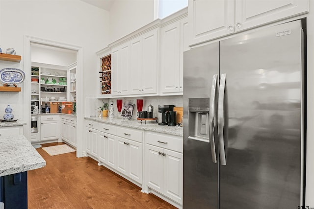 kitchen with backsplash, stainless steel fridge, light stone countertops, light hardwood / wood-style floors, and white cabinetry