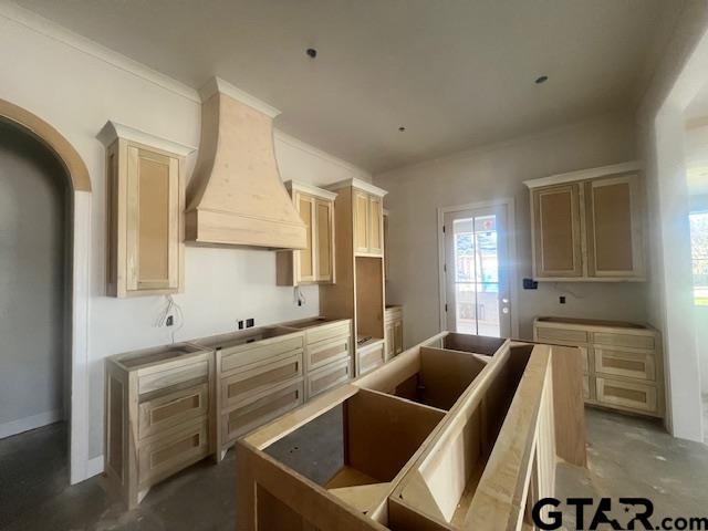 kitchen with concrete flooring, light brown cabinetry, a kitchen island, and premium range hood