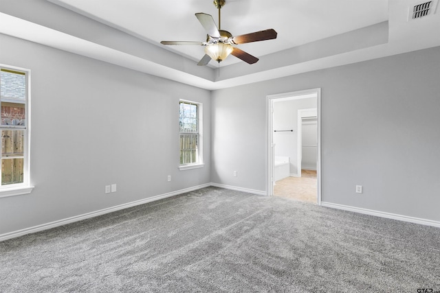 unfurnished bedroom with a walk in closet, carpet, ceiling fan, and a raised ceiling