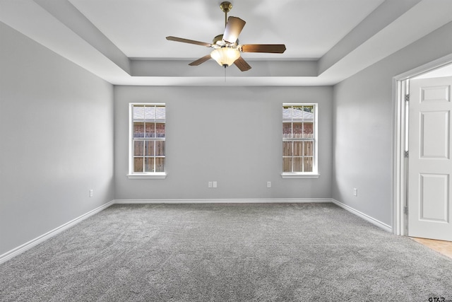 carpeted spare room featuring ceiling fan, a healthy amount of sunlight, and a raised ceiling