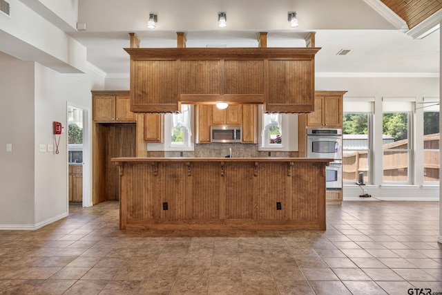 22886 County Road 422, Lindale, TX 75771 - kitchen featuring stainless steel appliances, tasteful backsplash, healthy amount of natural light, brown cabinets, and crown molding