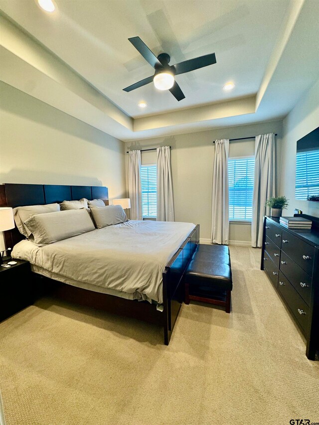 bedroom with multiple windows, light colored carpet, a raised ceiling, and ceiling fan