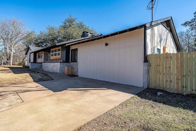 view of property exterior featuring stone siding, a patio area, driveway, and fence