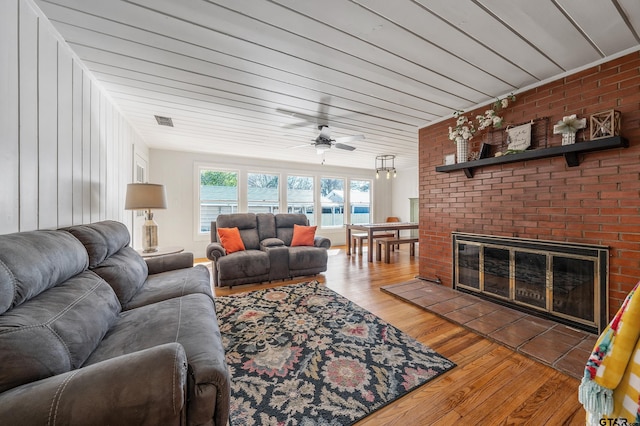 living room featuring a ceiling fan, a brick fireplace, visible vents, and wood finished floors