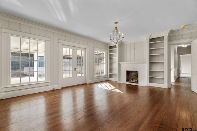 unfurnished living room with dark hardwood / wood-style floors, ornamental molding, a brick fireplace, built in shelves, and a chandelier