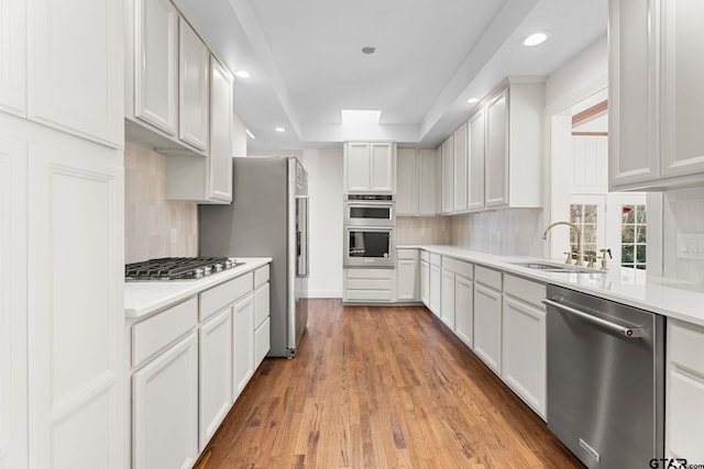 kitchen with sink, white cabinetry, backsplash, stainless steel appliances, and light hardwood / wood-style floors