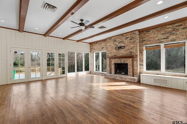 unfurnished living room with french doors, wood-type flooring, a brick fireplace, beamed ceiling, and ceiling fan