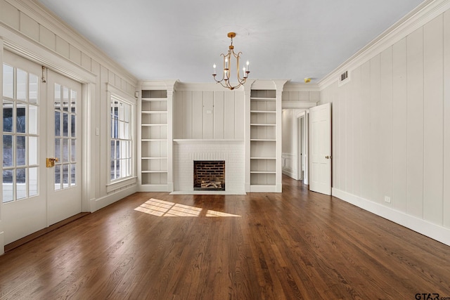 unfurnished living room with crown molding, dark hardwood / wood-style floors, a notable chandelier, a brick fireplace, and built in shelves