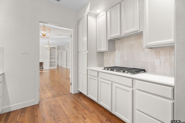 kitchen featuring hardwood / wood-style flooring, white cabinetry, a notable chandelier, stainless steel gas cooktop, and decorative backsplash