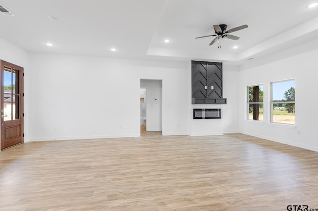 unfurnished living room with recessed lighting, a tray ceiling, a large fireplace, and a wealth of natural light