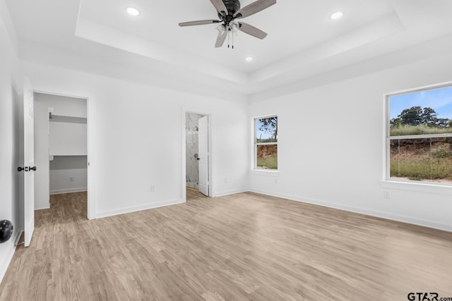 unfurnished bedroom with a tray ceiling, baseboards, light wood-style flooring, and a spacious closet