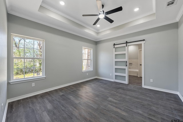 unfurnished bedroom with ceiling fan, a barn door, a raised ceiling, and multiple windows