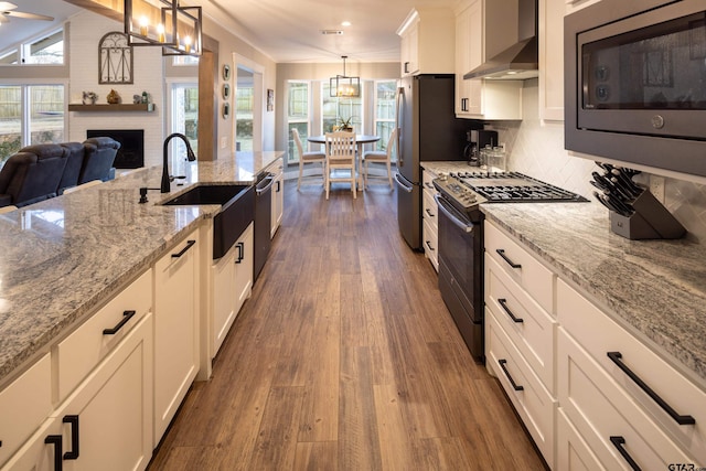 kitchen with pendant lighting, sink, white cabinets, stainless steel appliances, and wall chimney range hood