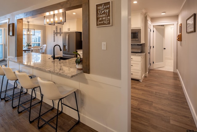 kitchen with pendant lighting, appliances with stainless steel finishes, white cabinetry, a kitchen breakfast bar, and light stone counters