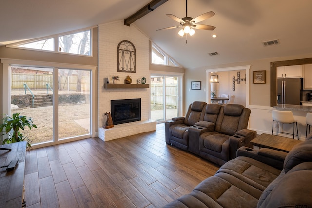 living room featuring high vaulted ceiling, beamed ceiling, hardwood / wood-style flooring, ceiling fan, and a brick fireplace