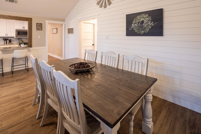 dining space with lofted ceiling, wooden walls, and dark hardwood / wood-style flooring