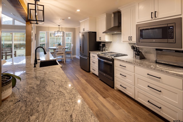 kitchen featuring pendant lighting, sink, white cabinetry, stainless steel appliances, and wall chimney exhaust hood