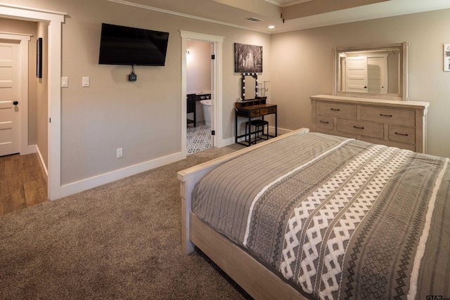 bedroom with crown molding, ensuite bath, and dark colored carpet