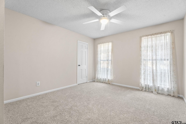 carpeted spare room featuring a textured ceiling, a wealth of natural light, and ceiling fan