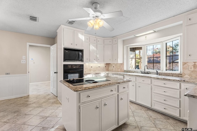 kitchen featuring black appliances, sink, tasteful backsplash, a kitchen island, and white cabinetry