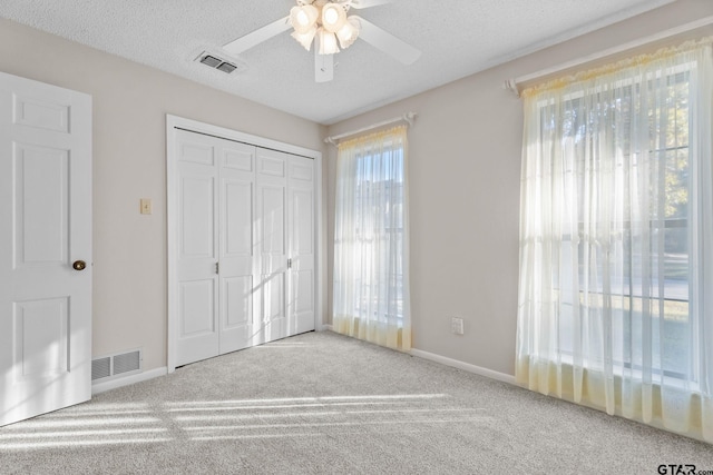 unfurnished bedroom featuring ceiling fan, a closet, light colored carpet, and a textured ceiling