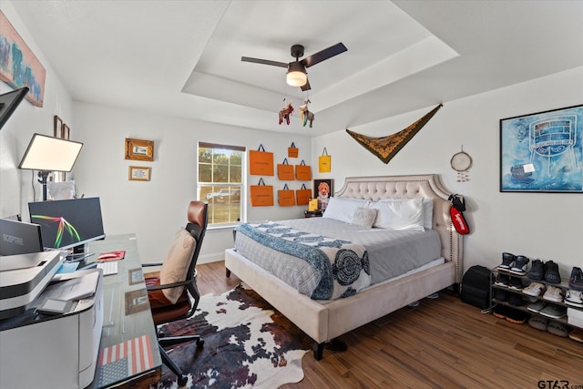 bedroom with dark hardwood / wood-style floors, ceiling fan, and a tray ceiling