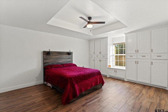 bedroom with ceiling fan, a closet, dark hardwood / wood-style flooring, and a tray ceiling