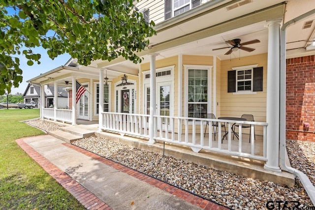 entrance to property featuring a porch, a ceiling fan, and a lawn