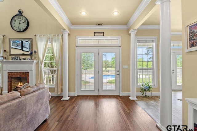 doorway to outside with a fireplace, a wealth of natural light, ornamental molding, and decorative columns