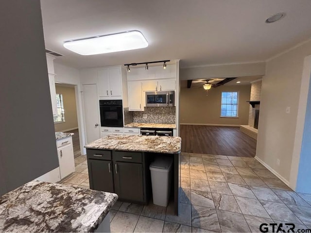 kitchen with light stone counters, a center island, ceiling fan, white cabinets, and decorative backsplash