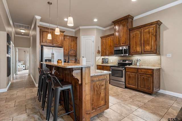 kitchen with appliances with stainless steel finishes, hanging light fixtures, light stone countertops, a center island with sink, and decorative backsplash