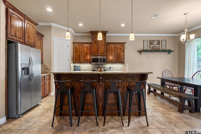 kitchen featuring light stone counters, pendant lighting, stainless steel appliances, and an island with sink