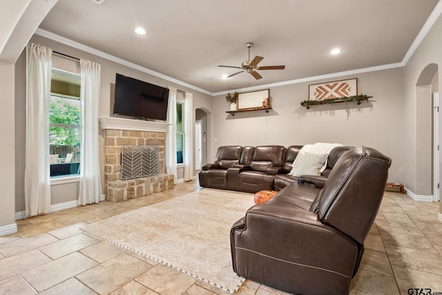 living room with a stone fireplace, ornamental molding, and ceiling fan