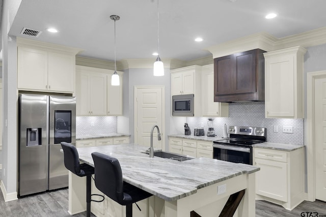 kitchen with sink, an island with sink, appliances with stainless steel finishes, decorative light fixtures, and light hardwood / wood-style floors