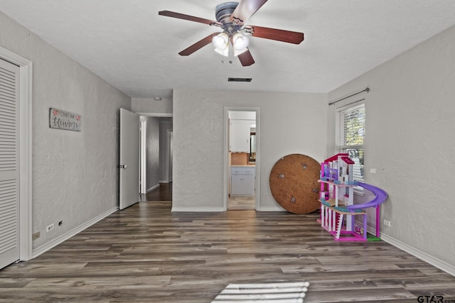 playroom featuring dark wood-type flooring, a textured ceiling, and ceiling fan