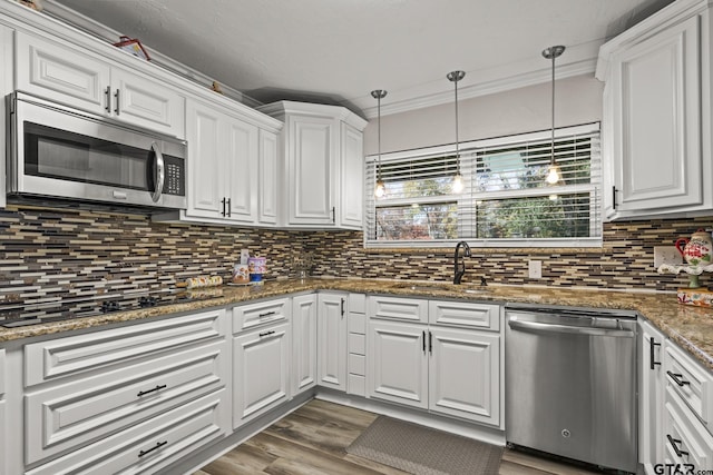 kitchen featuring pendant lighting, dark stone countertops, stainless steel appliances, ornamental molding, and white cabinets