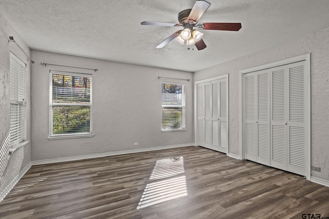 unfurnished bedroom with dark hardwood / wood-style flooring, two closets, and multiple windows