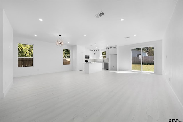 unfurnished living room featuring light hardwood / wood-style floors, a chandelier, and plenty of natural light