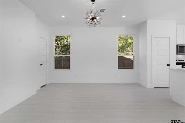 unfurnished room with light wood-type flooring, a notable chandelier, and a healthy amount of sunlight