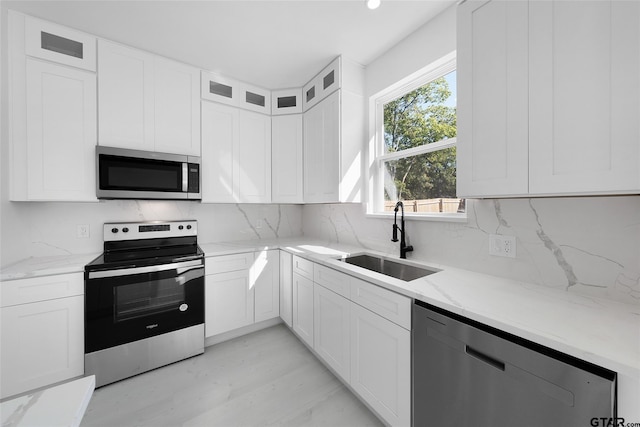 kitchen with light stone counters, backsplash, appliances with stainless steel finishes, sink, and white cabinets