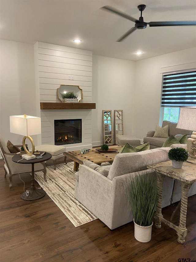 living room featuring ceiling fan, a large fireplace, and dark hardwood / wood-style floors