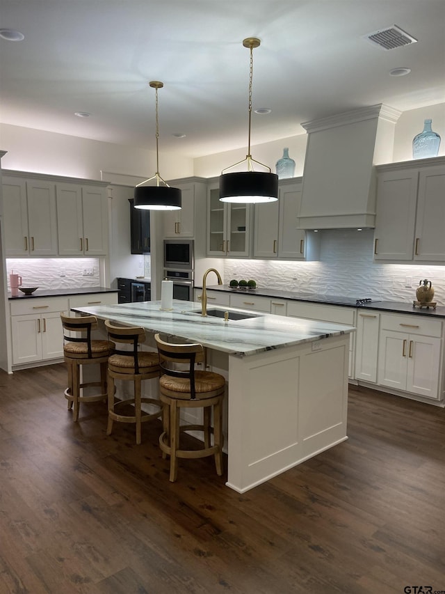 kitchen featuring tasteful backsplash, custom range hood, stainless steel appliances, a kitchen island with sink, and sink