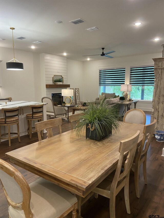 dining space featuring ceiling fan, a large fireplace, and dark wood-type flooring