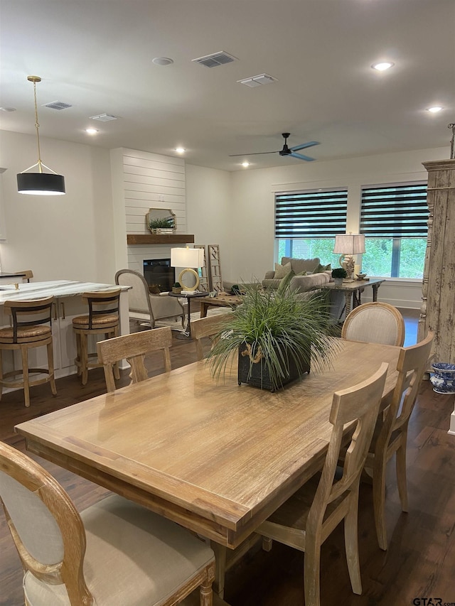 dining area featuring dark wood-type flooring, a large fireplace, and ceiling fan