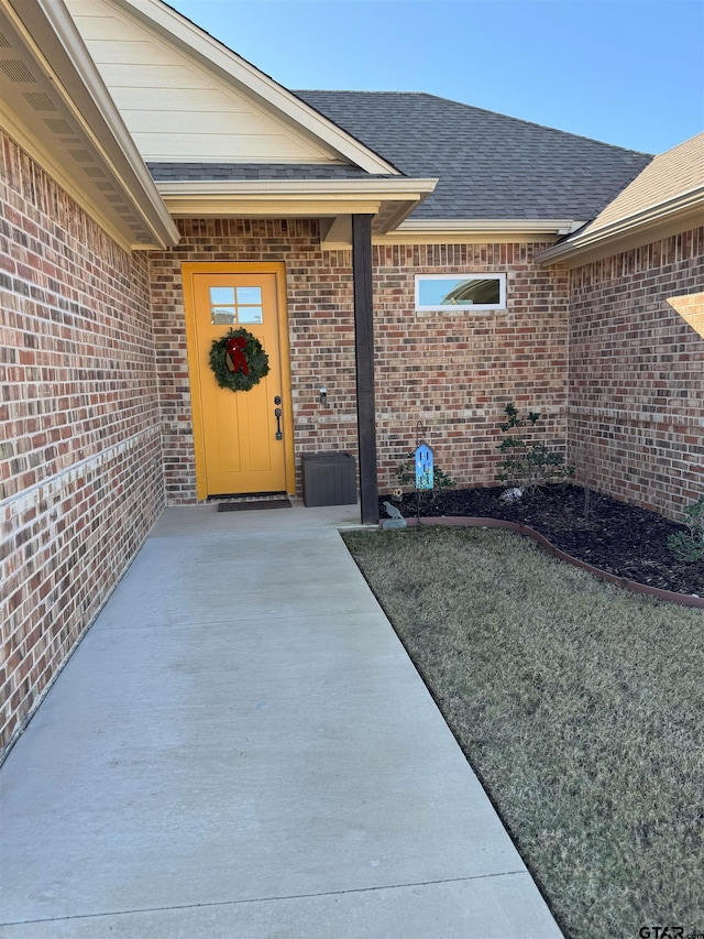 entrance to property featuring brick siding and roof with shingles