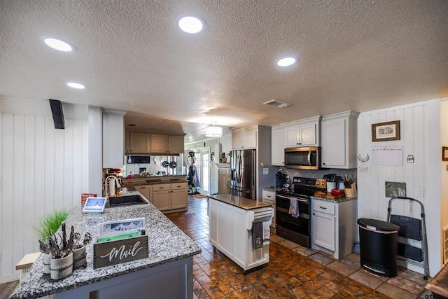 kitchen featuring a textured ceiling, appliances with stainless steel finishes, a center island, wooden walls, and sink