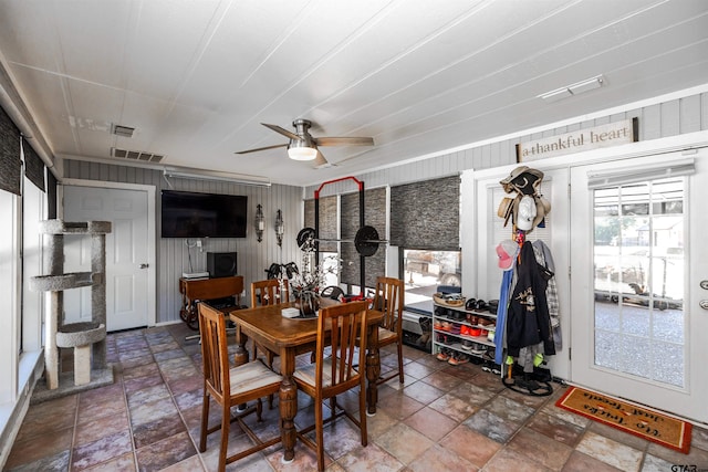 dining space featuring ceiling fan and wood walls