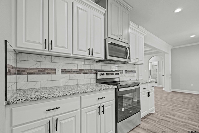 kitchen with tasteful backsplash, light stone countertops, white cabinetry, light wood-type flooring, and appliances with stainless steel finishes